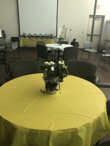 Round dining table covered with gold tablecloth and flower centerpiece.